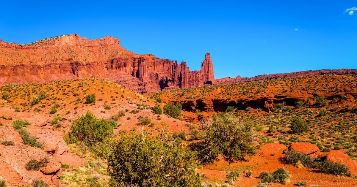 ed sandy expanse with low shrubs, red stone mesa and rock formations, blue sky